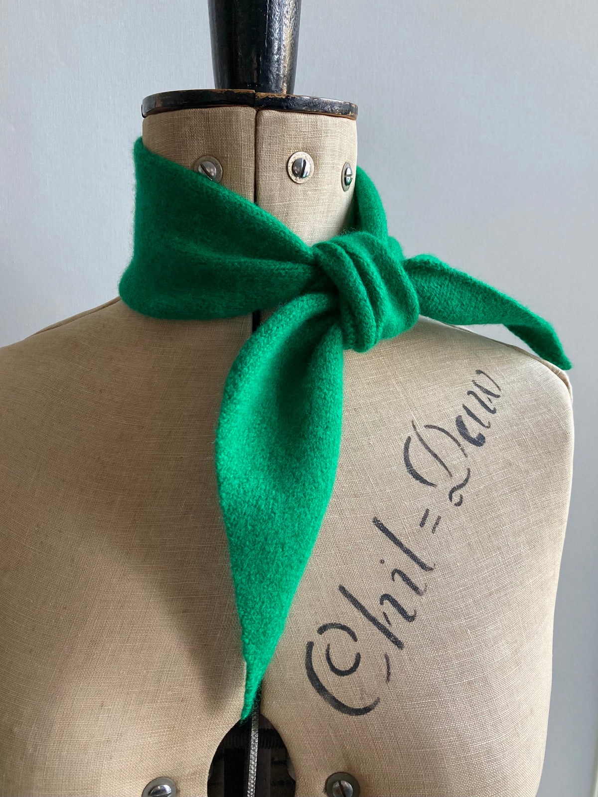 A bright green knitted thin neck scarf tied around a mannequin.