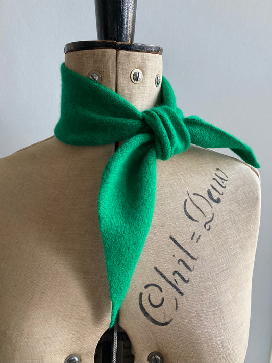 A bright green knitted thin neck scarf tied around a mannequin.