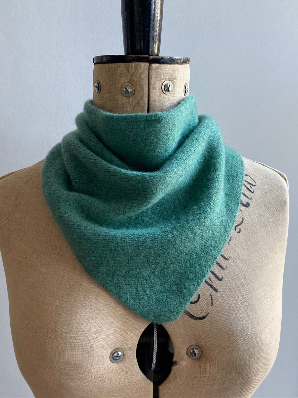 A sea green knitted triangle scarf bandana styled on a mannequin.