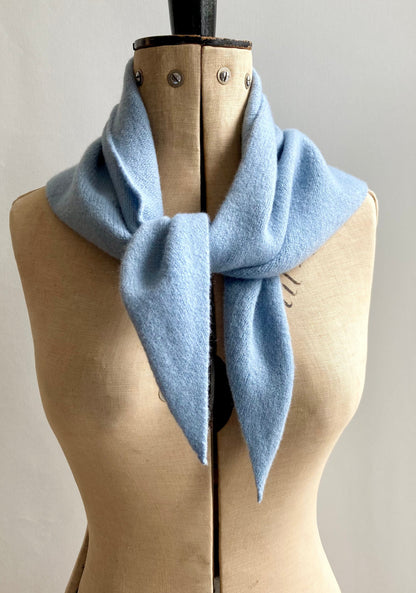 A pale blue knitted wool triangle scarf styled on a mannequin.