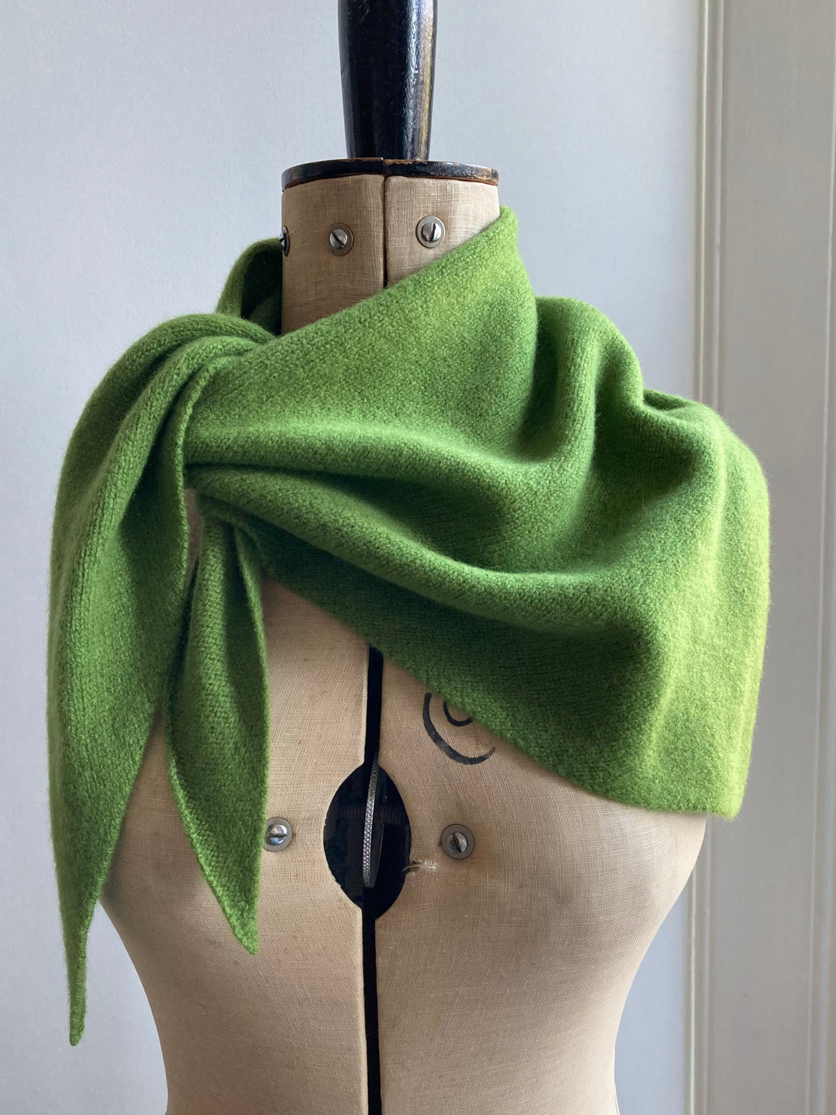A bright green knitted triangle scarf draped and tied on a mannequin.