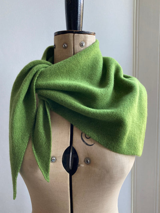 A bright green knitted triangle scarf draped and tied on a mannequin.