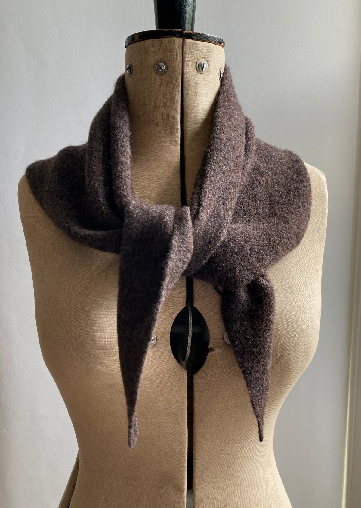 A dark brown knitted neckerchief scarf wrapped around a mannequin. 