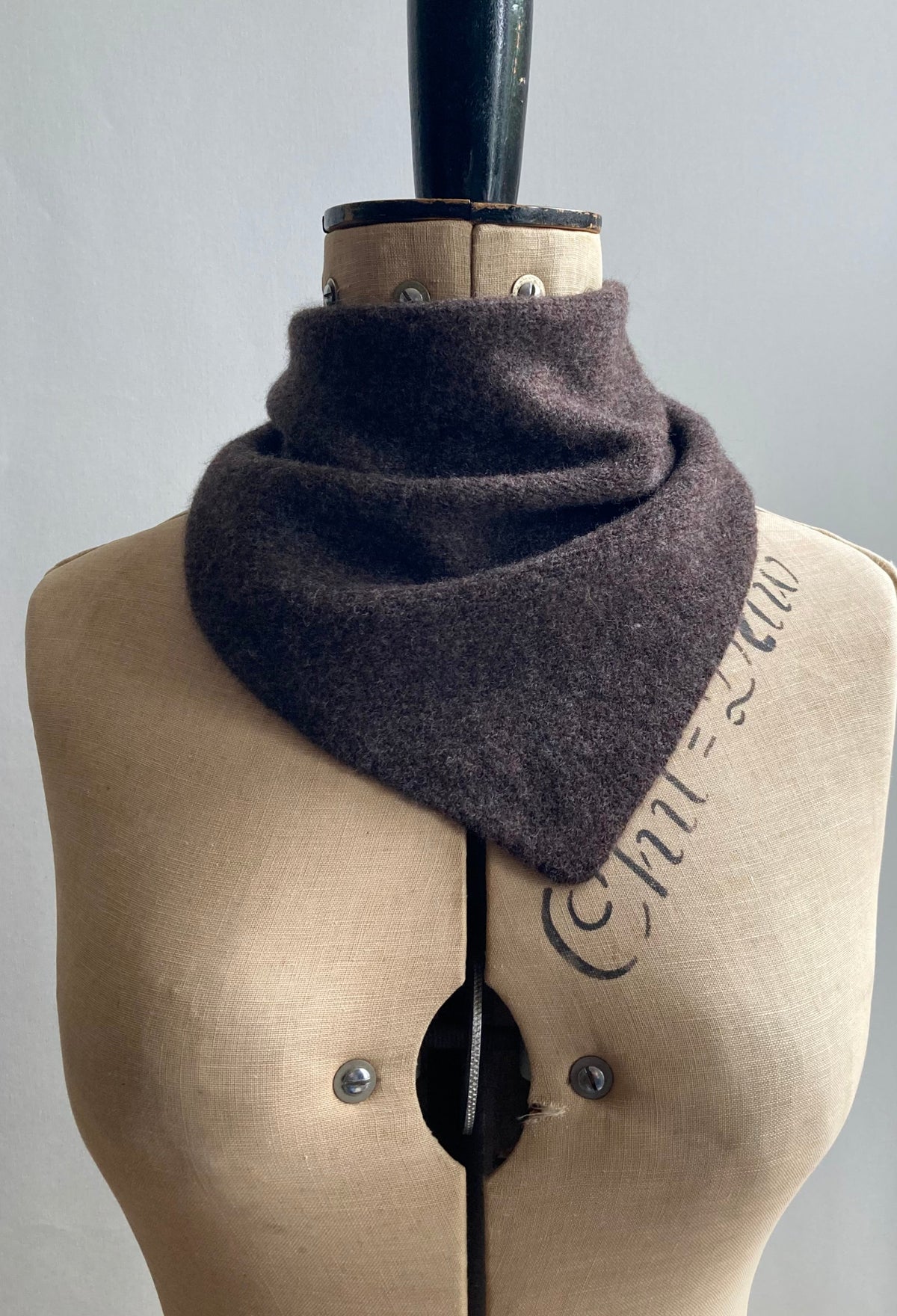 A dark brown knitted triangle neck scarf styled on a mannequin.