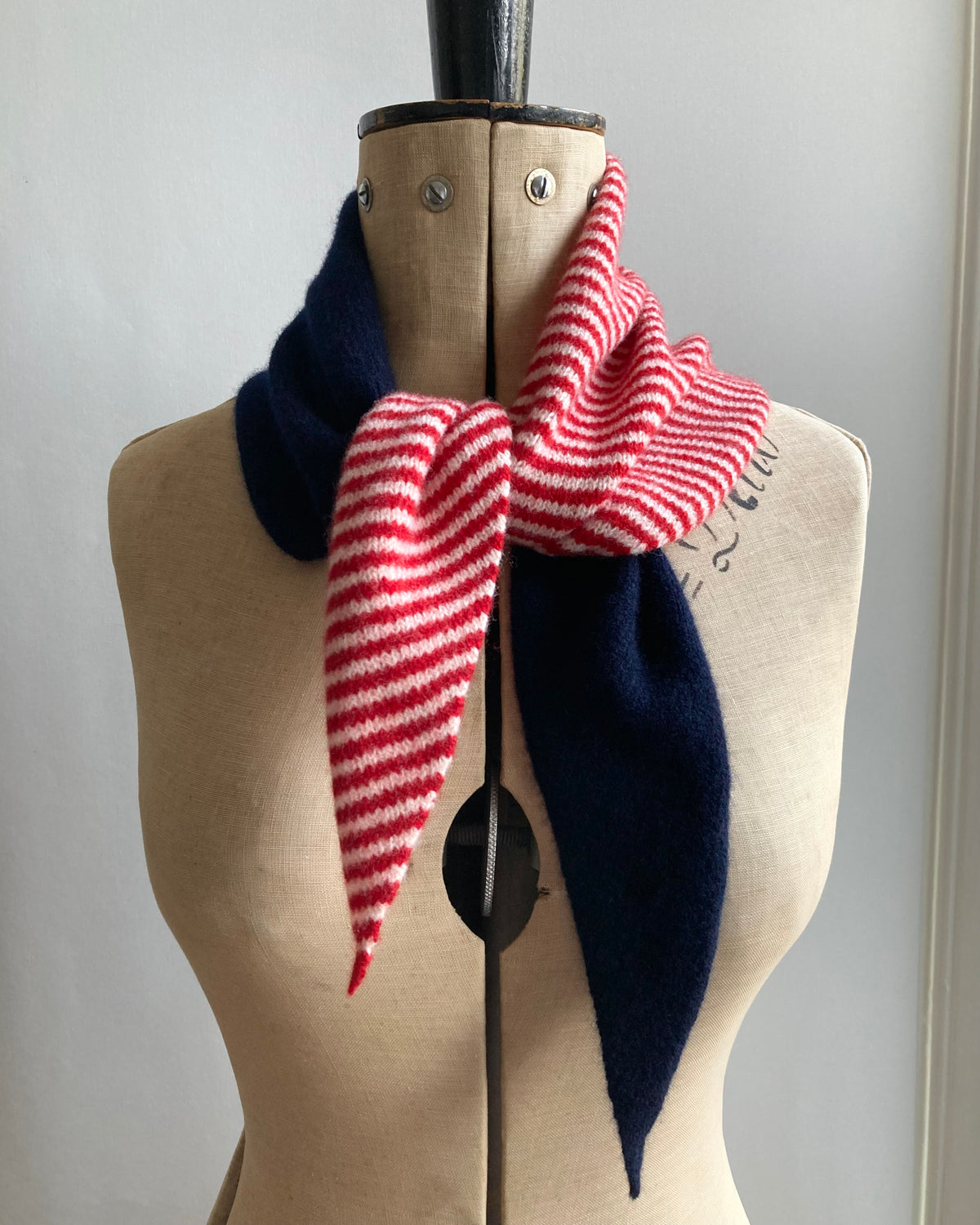 A knitted neck scarf, half navy - half red and white stripes, tied on a mannequin.