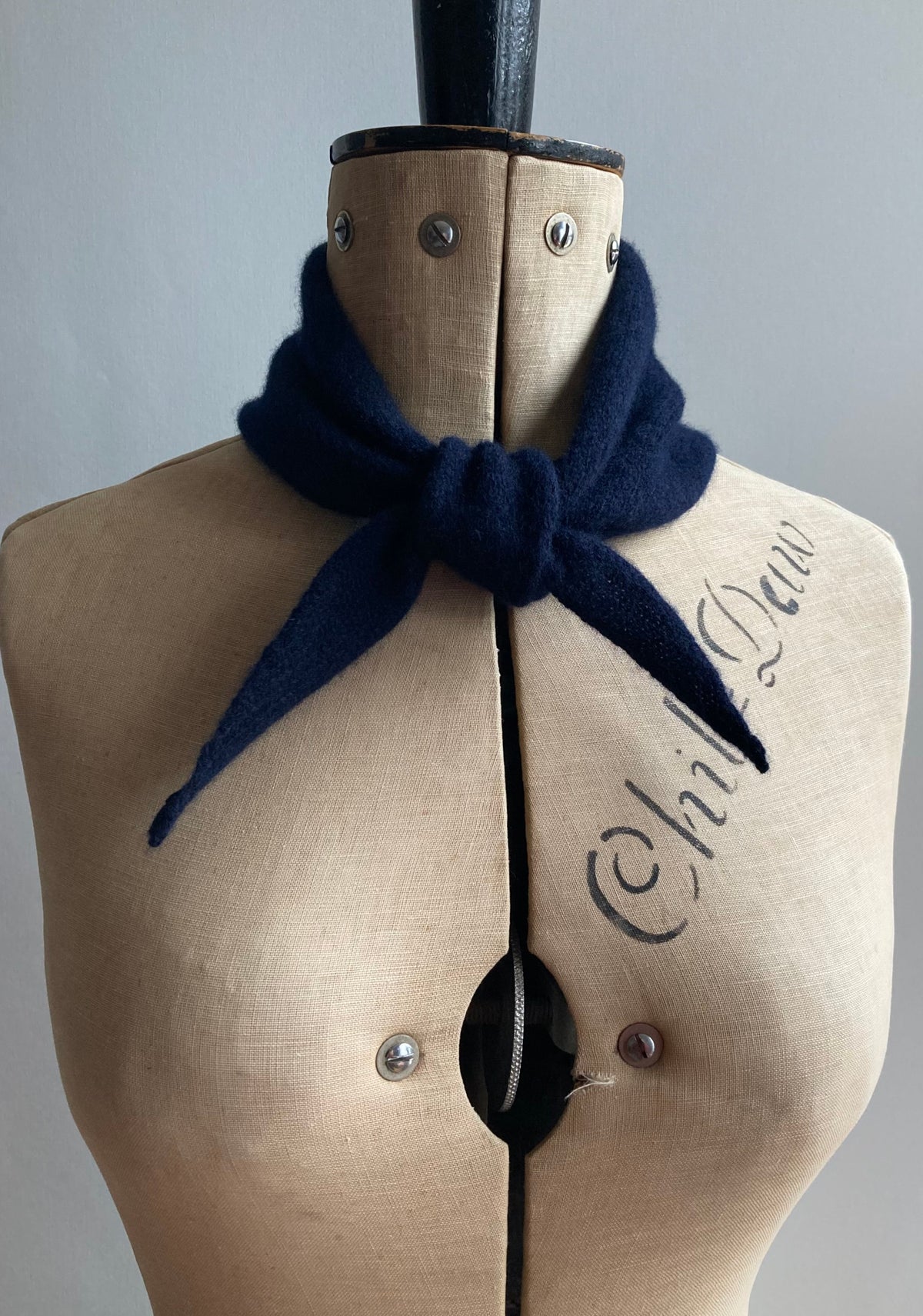 A dark navy knitted mini bandana scarf tied in a knot around a mannequin.
